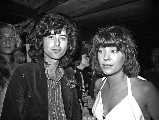 Black and white photo of Jimmy page in a suit jacket with long hair, and Pamela Des barres, in a white shirt.