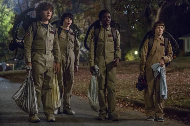Colored movie still of four boys dressed up as the Ghostbusters in Stranger Things.