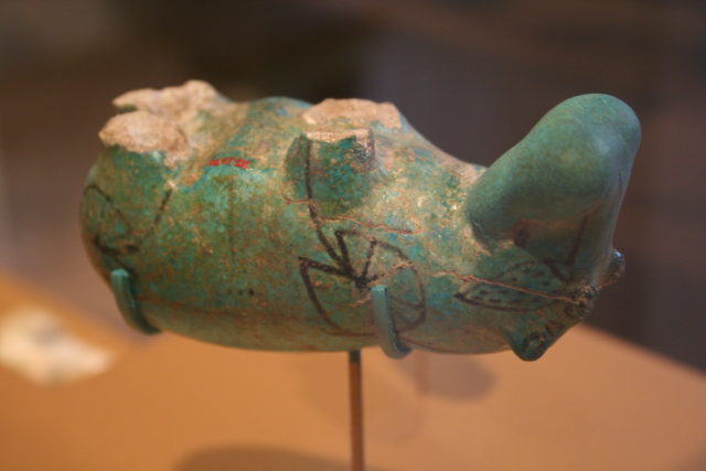 Coloured photo of a turquoise hippopotamus statue turned upside down and missing legs.