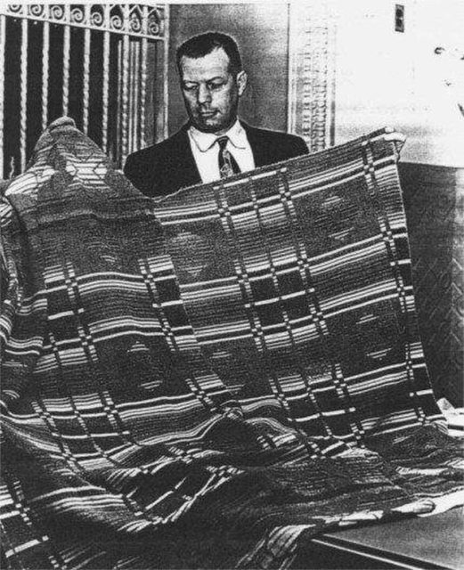 Man holding up a large plaid blanket