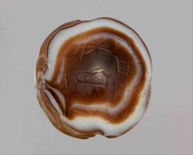 White and orange striped bead with cuneiform characters faintly on the top.