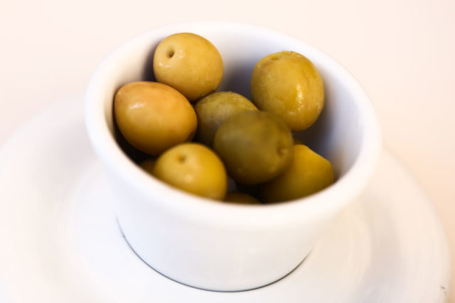 Colored photo of a white bowl with green olives in it.