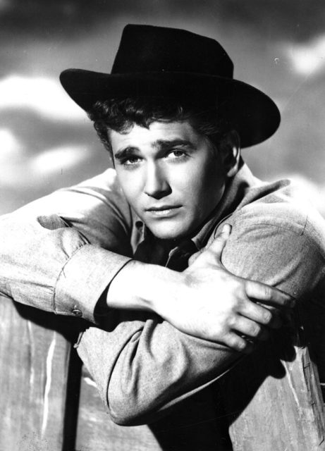 Black and white photo of Michael Landon leaning against a post while wearing a cowboy hat 