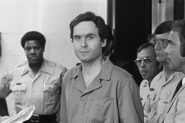 Ted Bundy in a prison uniform surrounded by police officers while on trial