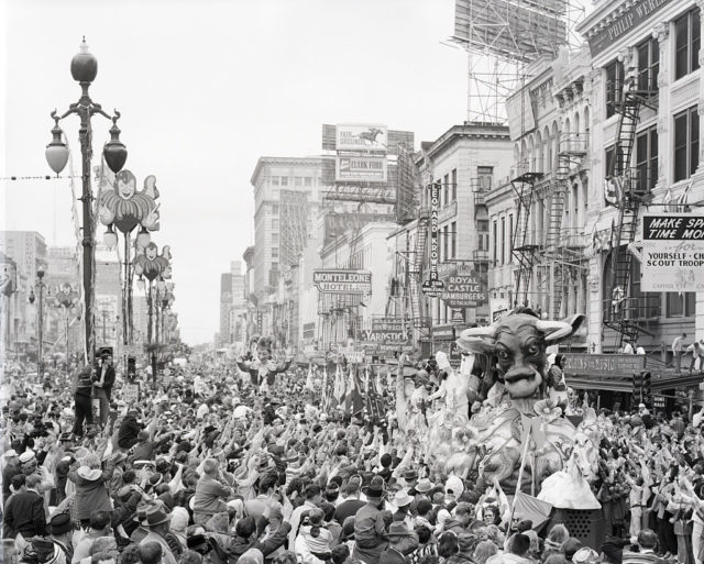 Black and white photo of a float with a bull head moving through a large crowd.