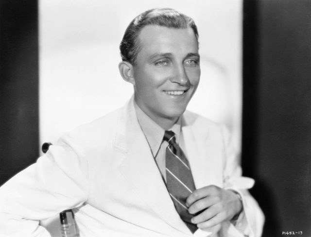 Black and white photo of Bing Crosby in a suit and tie, holding his tie.