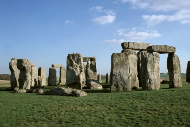 View of the rocks at Stonehenge with blue skies in the background and green grass.