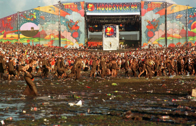 Woman wading through a large puddle of mud while music fans gather around the Woodstock '99 stage