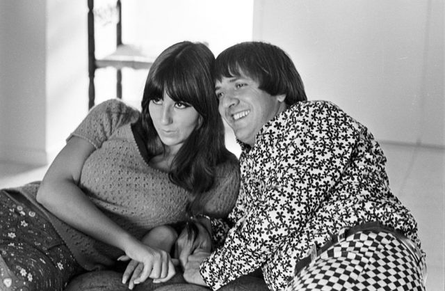 Black and white photo of Sonny and Cher lying down, propped up on their elbows during a photoshoot.