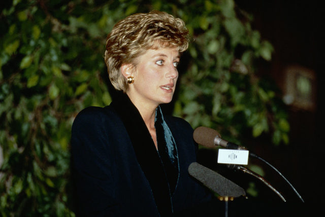 Colored photo of Princess Diana standing behind a microphone speaking to a crowd. 