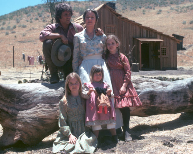 Colored photo from 'Little House on the Prairie' with the cast sitting on a fallen tree.