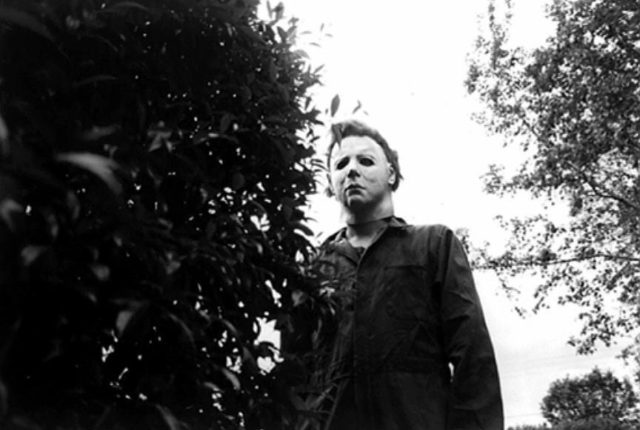 Michael Myers looks at the camera from behind a bush