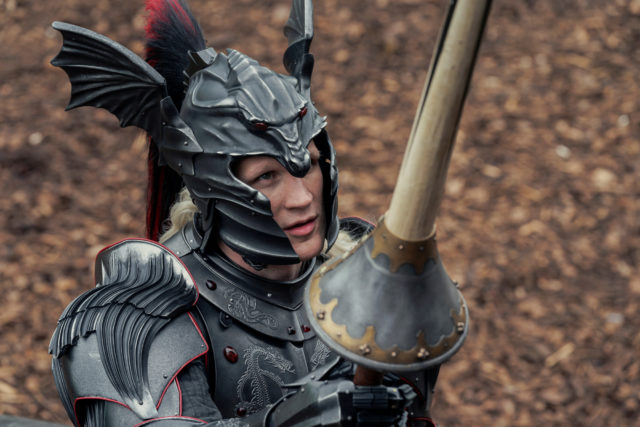 Color film still of Matt Smith carrying a lance, wearing armor and a helmet.