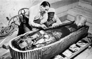 Black and white photo of Howard Carter leaning over King Tuts sarcophagus inspecting it.