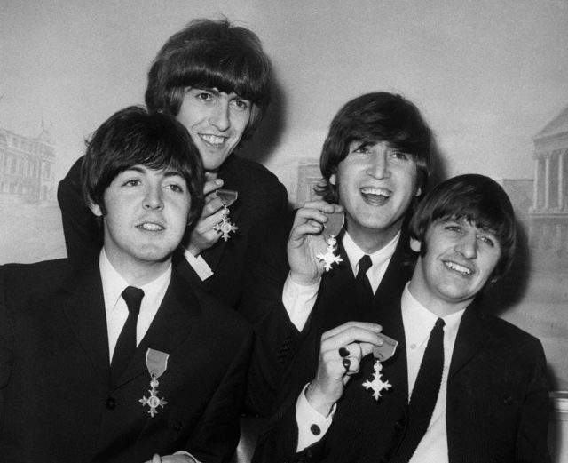The Beatles holding up their Most Excellent Order of the British Empire medals