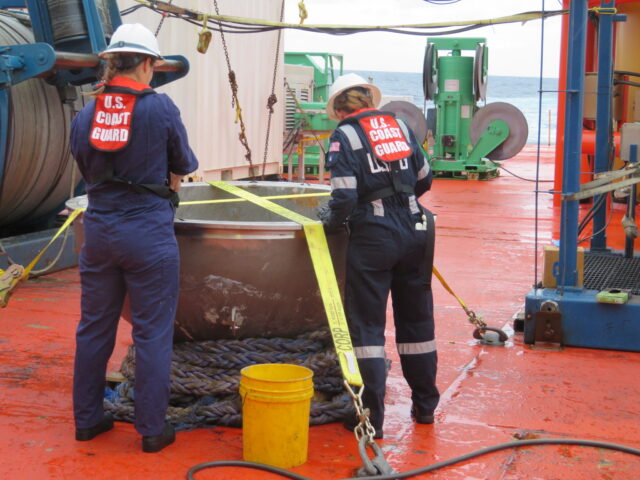 Two members of the US Coast Guard standing around a piece of debris from the Titan submersible