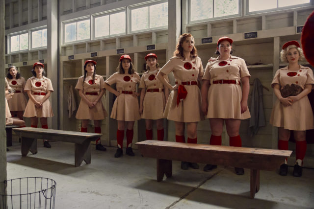 Women wearing dresses with long songs and baseball hats, standing in a locker room.