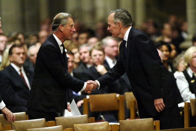King Charles III and President Bush both in black suits shake hands.