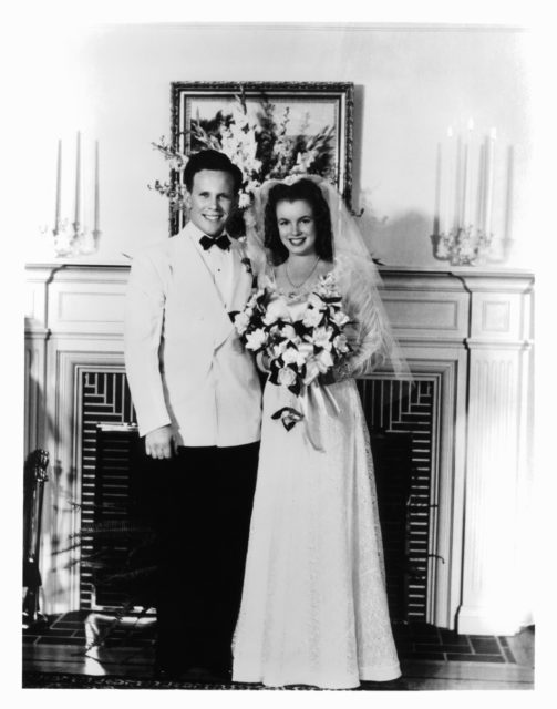 James Dougherty and Marilyn Monroe posing in front of a fireplace in their wedding attire