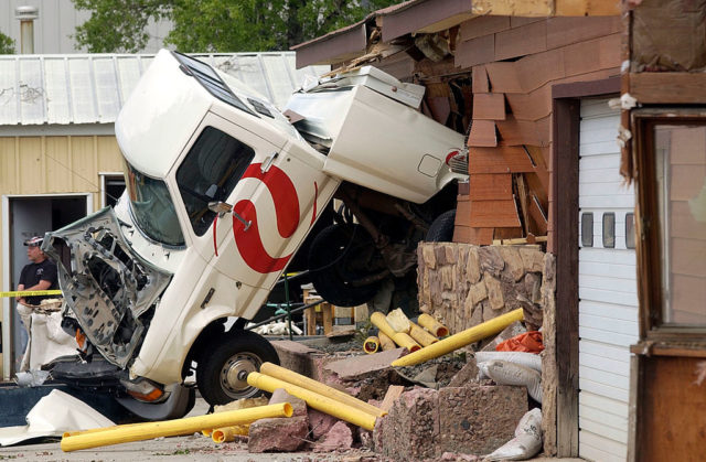 White truck stuck in the side of a destroyed red brick building.