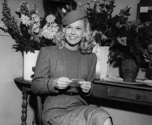 Doris Day holds a card while sitting in front of flowers