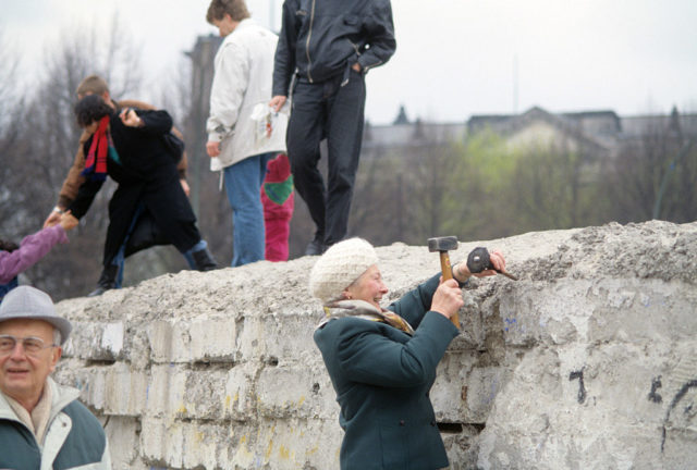 A woman uses a hammer to chip away the Berlin Wall