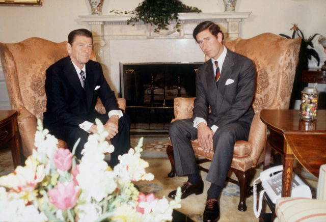 President Reagan in a black suit and King Charles III in a grey suit sit beside each other in high back chairs.