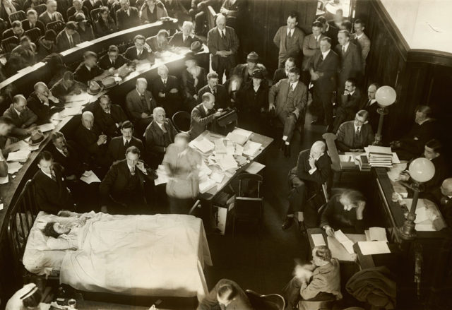 Jane Gibson lies in a bed in the middle of a courtroom surrounded by men in suits.