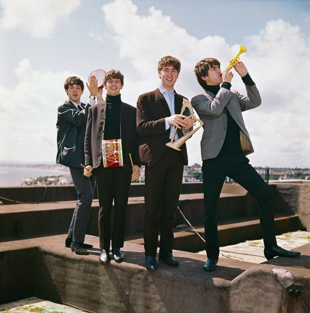 The Beatles holding various instruments while standing on the roof of the Palace Court Hotel