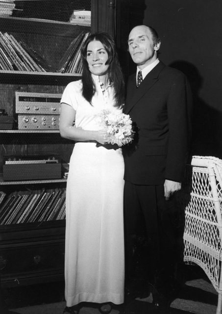 Gallo in a suit and tie beside Sina Essary in a white wedding dress holding flowers, at their wedding reception.