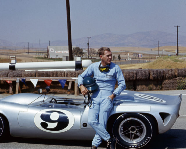 Steve McQueen sitting against a car