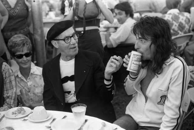 Groucho Marx and Alice Cooper sitting at a table in conversation.