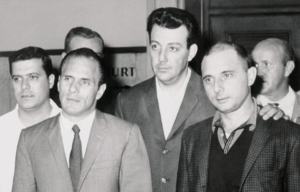 Joe Gallo in a suit walking beside his brother Larry Gallo in a group of people.