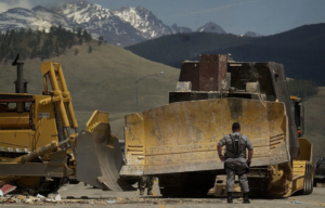 Man standing in front of an armored bulldozer with mountains in the background.