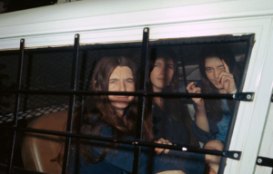 The three female members of Charles Manson's "family" pose for photographers through the window of the sheriff's van as they arrive at the courthouse to continue the murder trial in the Tate-LaBianca case. Patricia Krenwinkle (left) makes a face as Leslie Van Houten and Susan Atkins (right) smile, August 5, 1970.