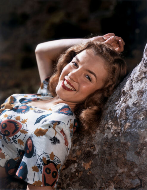 a young Marilyn Monroe leaning against a tree