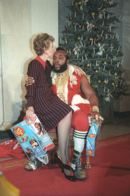 Nancy Reagan kissing Mr. T on the head, sitting on his lap, while he is dressed like Santa.