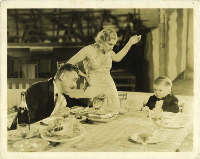 A man and woman speak to a small person at a dining room table