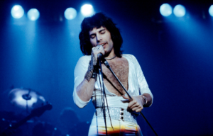 Freddie Mercury in a white, open-chested shirt, singing into a microphone