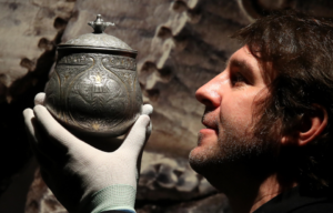A man holds a silver jar before his face