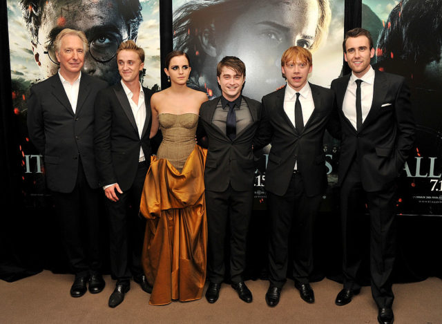 Alan Rickman, Tom Felton, Emma Watson, Daniel Radcliffe, Rupert Grint and Matthew Lewis stand side by side in dress clothing at a movie premiere.