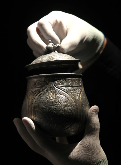 A silver jar with a lid being held by gloved hands
