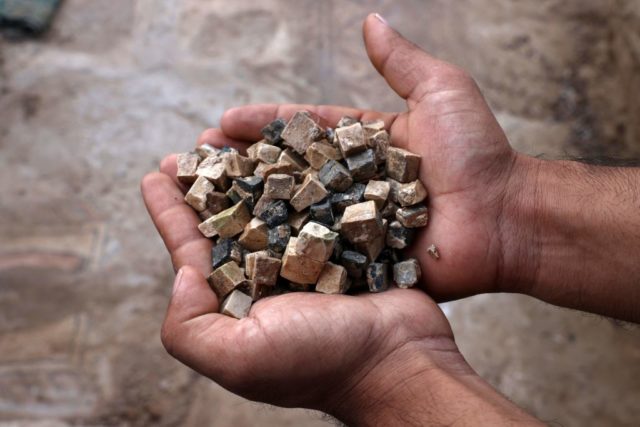 Hands holding broken, square pieces of tile that came from a mosaic. 