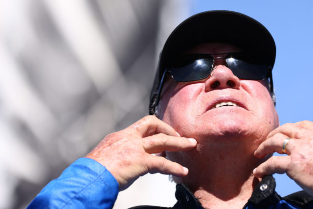 William Shatner in a hat and sunglasses scratching at his neck