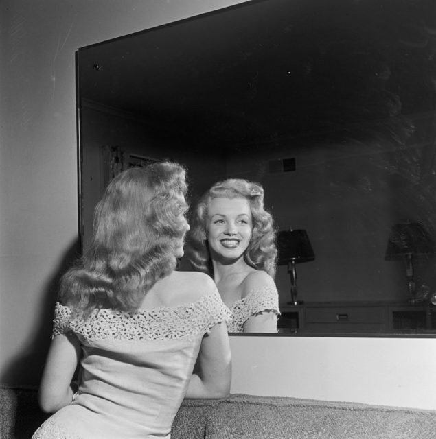 Marilyn Monroe smiles at her reflection in a mirror