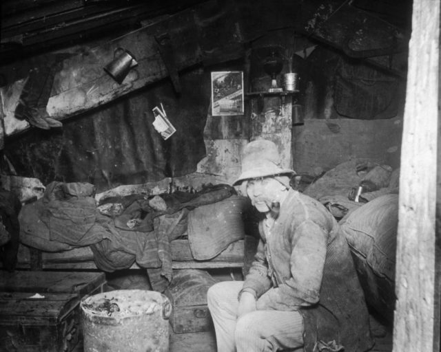 An old man sits next to a makeshift sleeping area