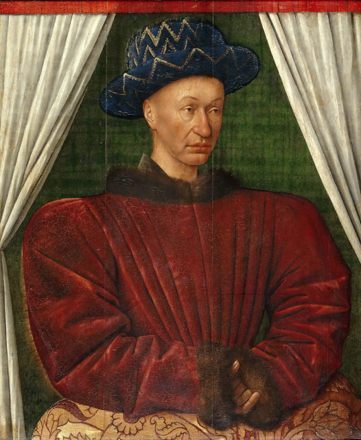 King Charles VII of France wearing a red top with puff sleeves, and a blue hat on his bald head.