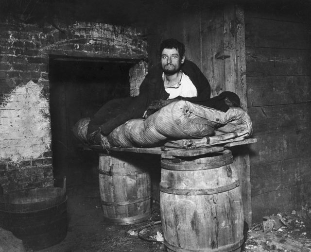 A homeless man sleeps on a plank balanced between two barrels
