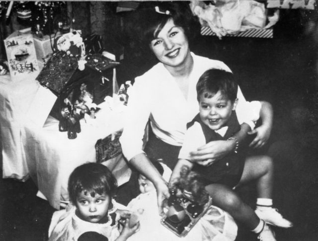 A family portrait with a mother holding a child on her lap, another baby looks away