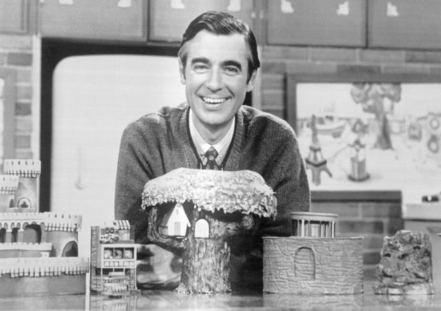 Mr. Rogers sitting smiling behind a model of a castle and tree.